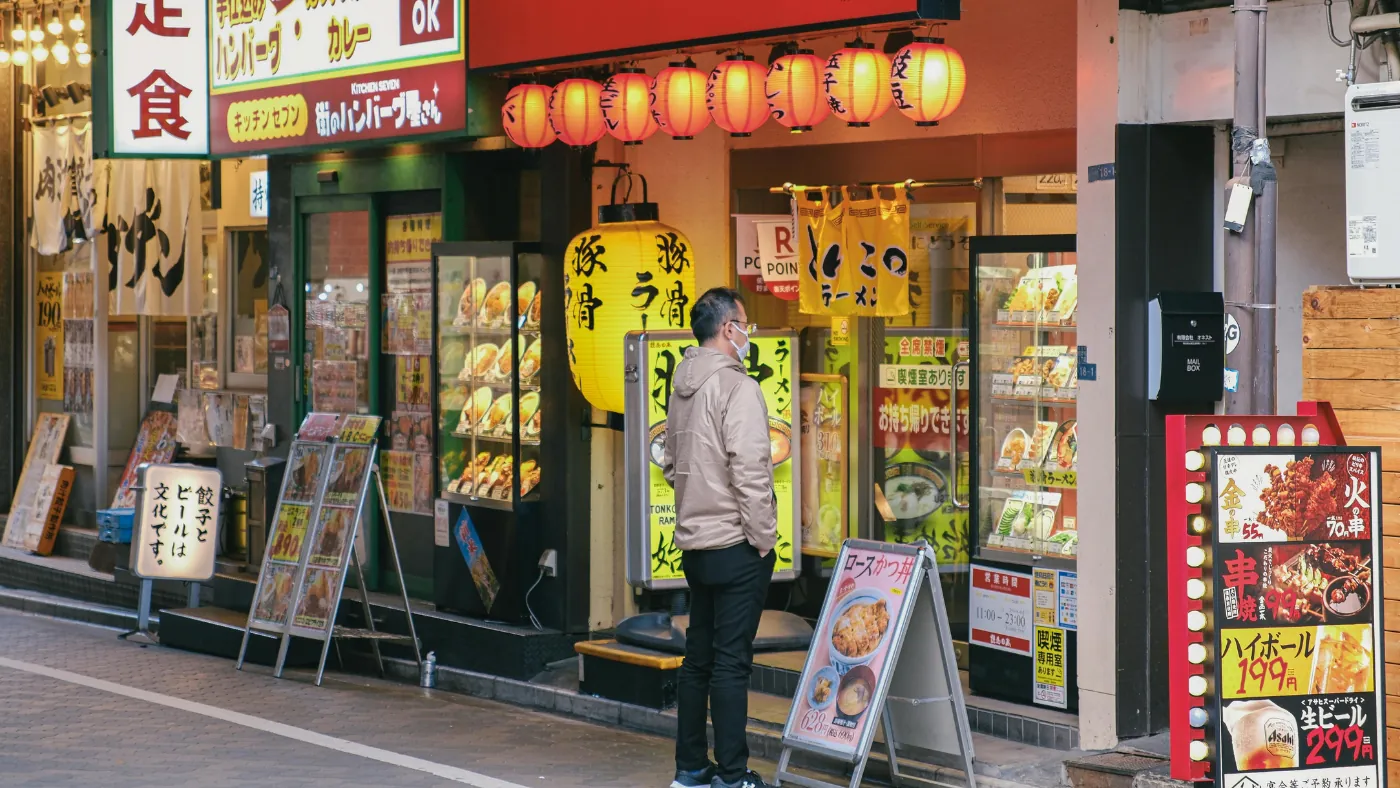 日本の飲食店が並ぶ路面。赤い提灯と食品サンプルのケースの前で、看板を見ている人