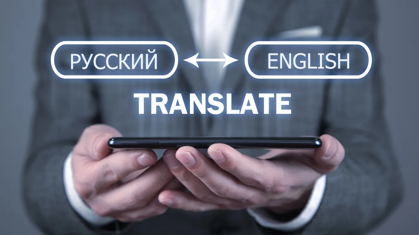 スマートフォンを両手で持つ人。画面の上に「РУССКИЙ ↔ ENGLISH TRANSLATE（ロシア語と英語を翻訳する）」の文字