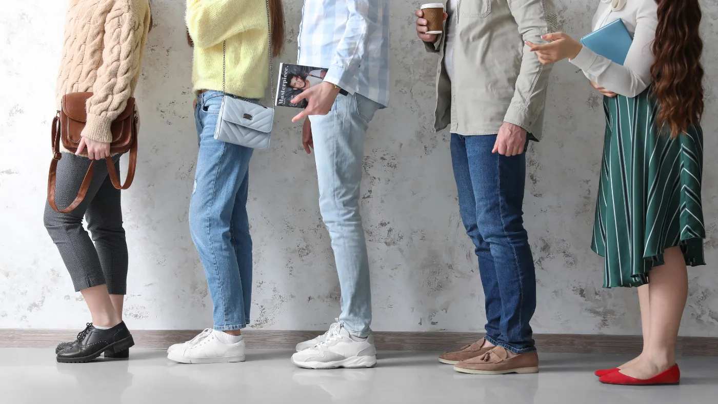 壁ぎわに5人が縦に並んでいる脚元。コーヒーカップや雑誌を持っている