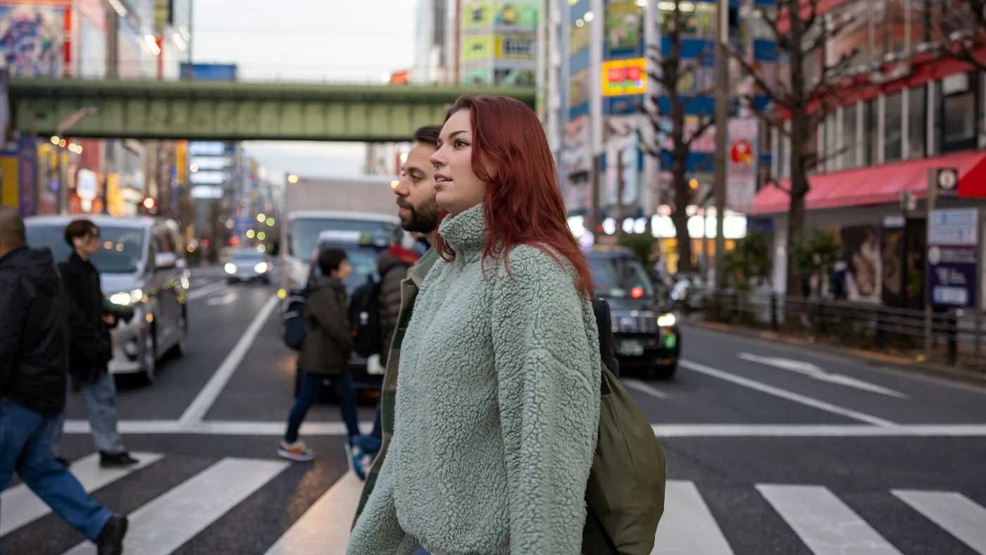 東京の繁華街の横断歩道を渡る外国人の男女。背景に看板とビルが並ぶ