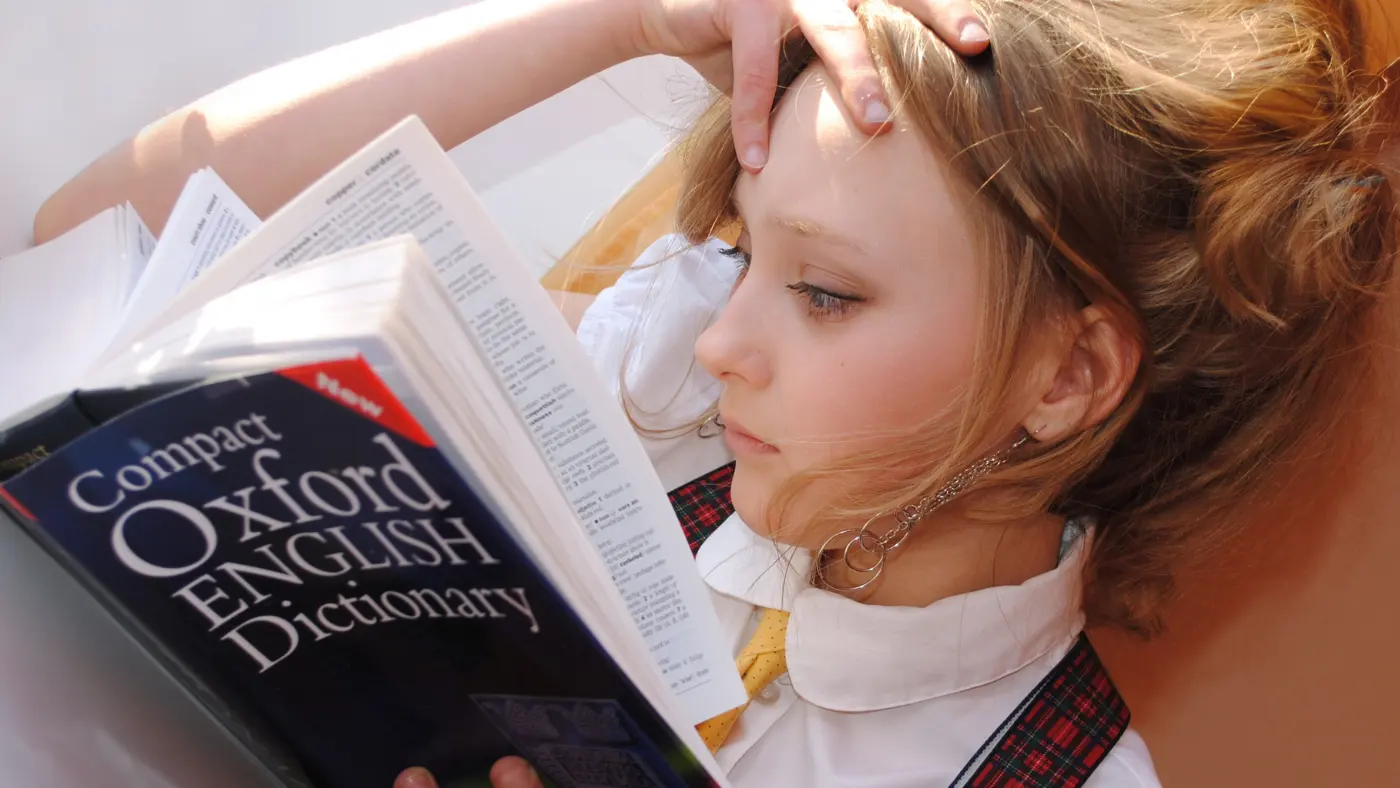 英語の辞書（Compact Oxford English Dictionary）を開き、頭に手を当てて読んでいる女性
