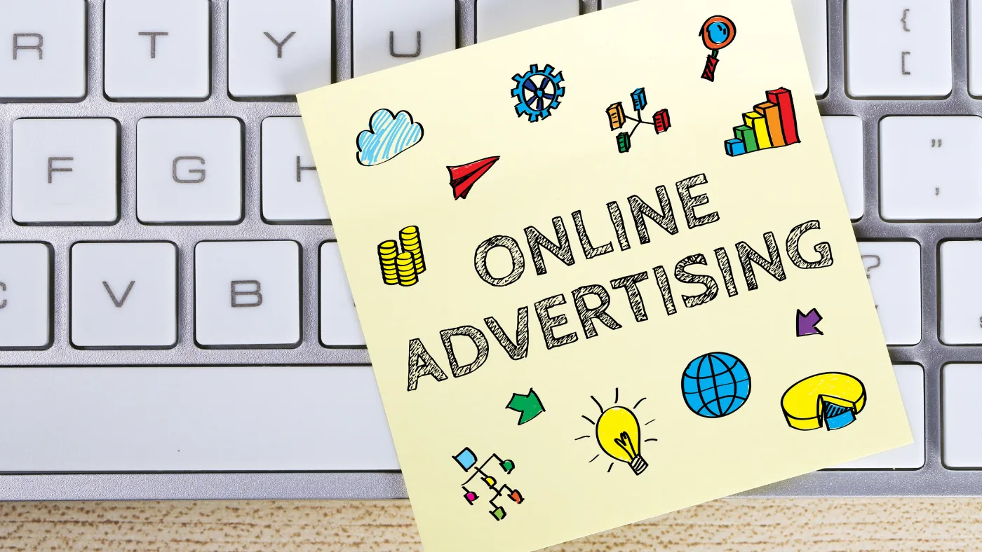 キーボードの上に置かれた黄色いふせん。ONLINE ADVERTISING の文字のまわりに、グラフ・電球・地球儀などのイラストが描かれている