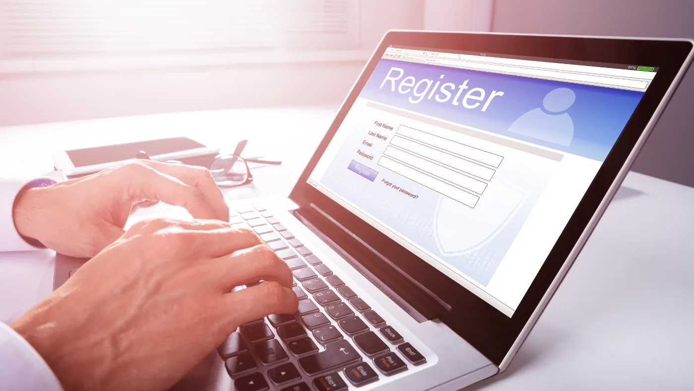 ノートパソコンの画面に「Register」と書かれた登録フォームが開かれ、両手でキーボードを打っている