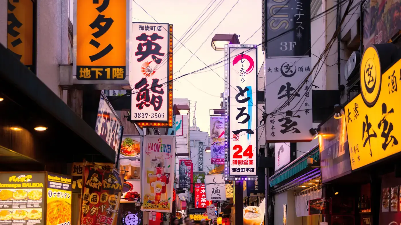 夕方の日本の繁華街。飲食店の縦長の看板が、通りの両側に並んでいる