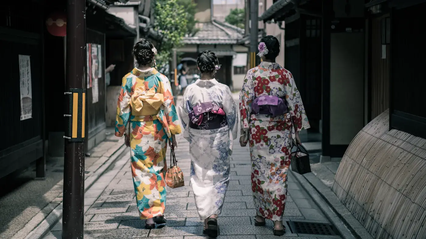 着物姿で石畳の路地を歩く3人の後ろ姿
