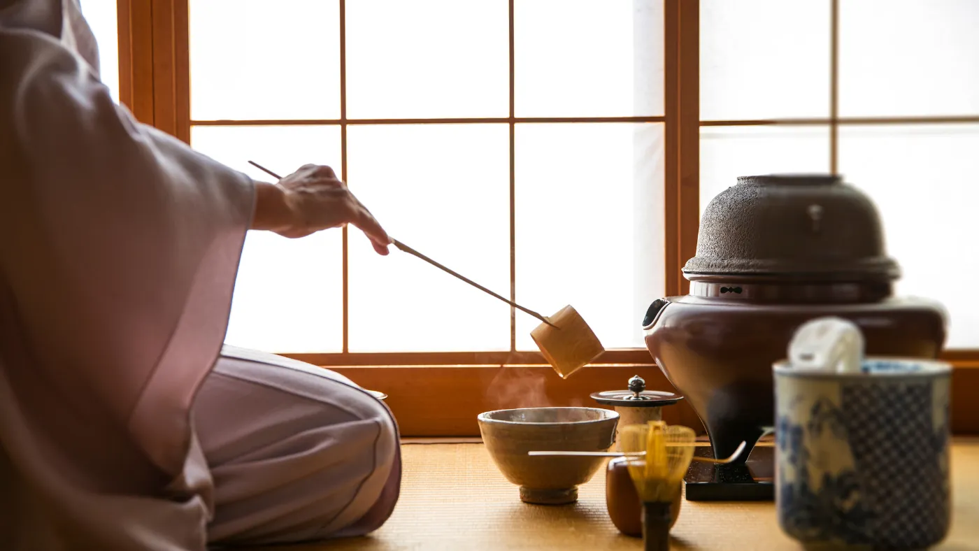 和室で、柄杓を使って茶を点てている手元と茶器