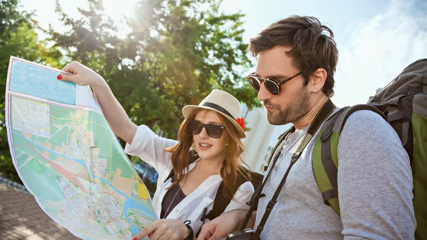バックパックを背負った男女の旅行者が、街なかで大きな地図を広げて行き先を確かめている
