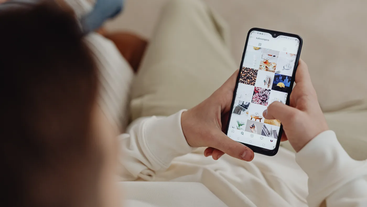 ソファに座った人が、写真が並んだInstagramの画面をスマートフォンで見ている手元