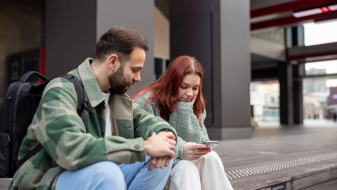 街角に座ってスマートフォンの画面を一緒に見ている外国人の2人連れ
