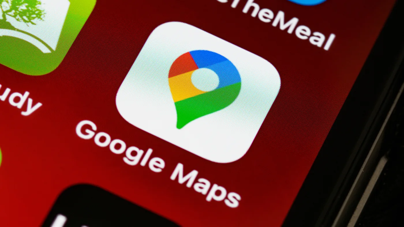 赤い背景のスマートフォンの画面に並んだアプリのうち、Google Mapsのアイコンを大きく写した写真