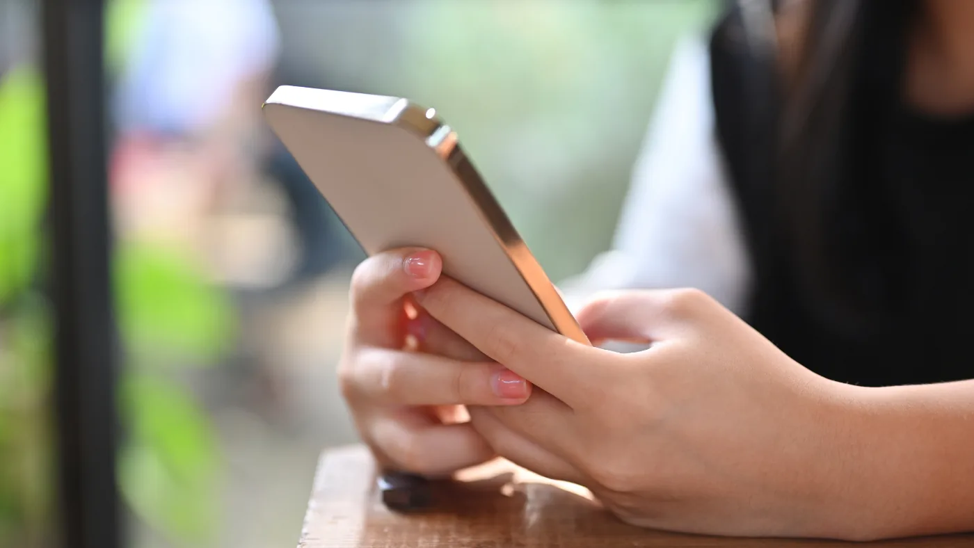 窓際の席でスマートフォンを両手で持って操作している手元